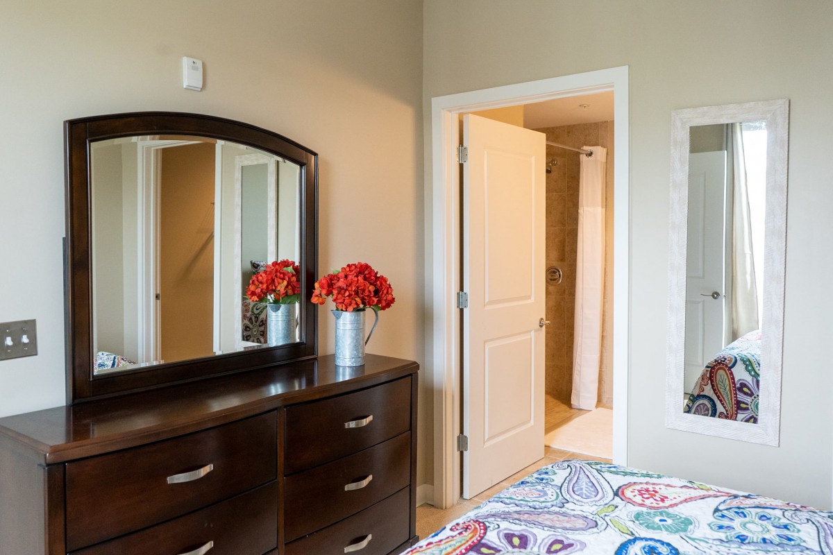 A cozy bedroom with a dresser and mirror, featuring bright red flowers for decoration.