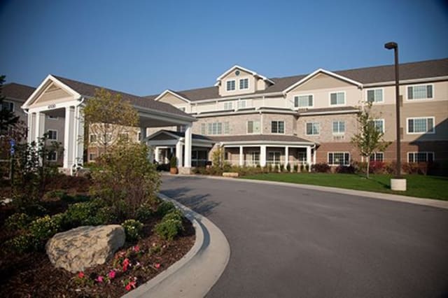 A large residential building with a landscaped entrance and driveway under a clear blue sky.