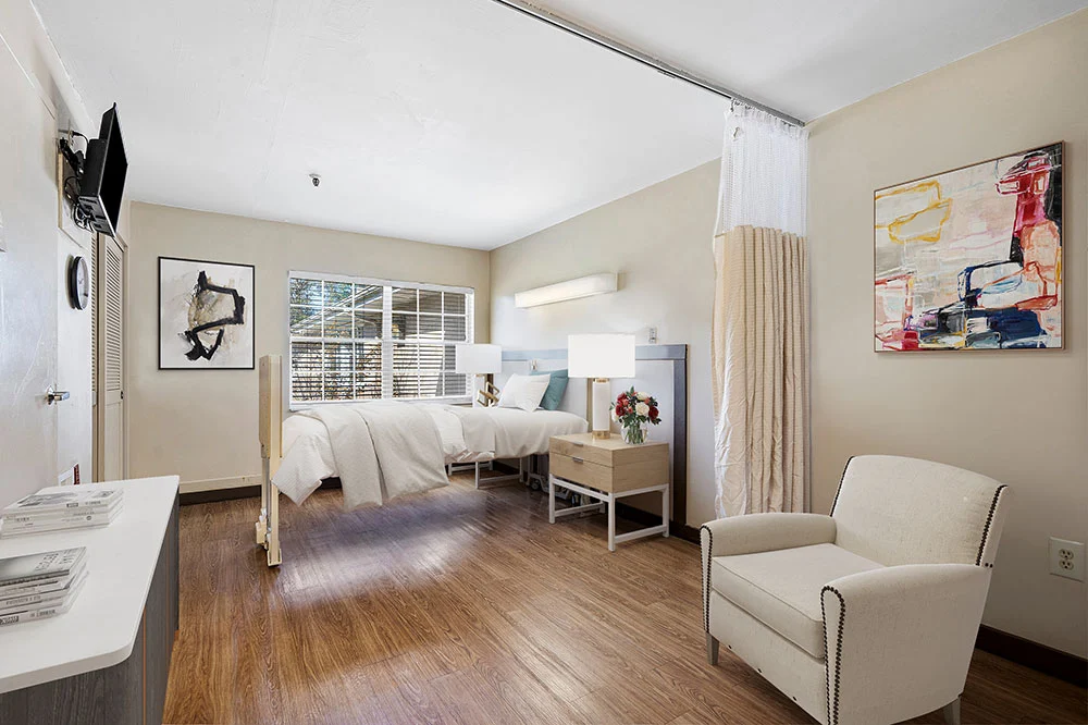 A modern hospital room with a bed, curtain divider, and a comfortable chair by the window.
