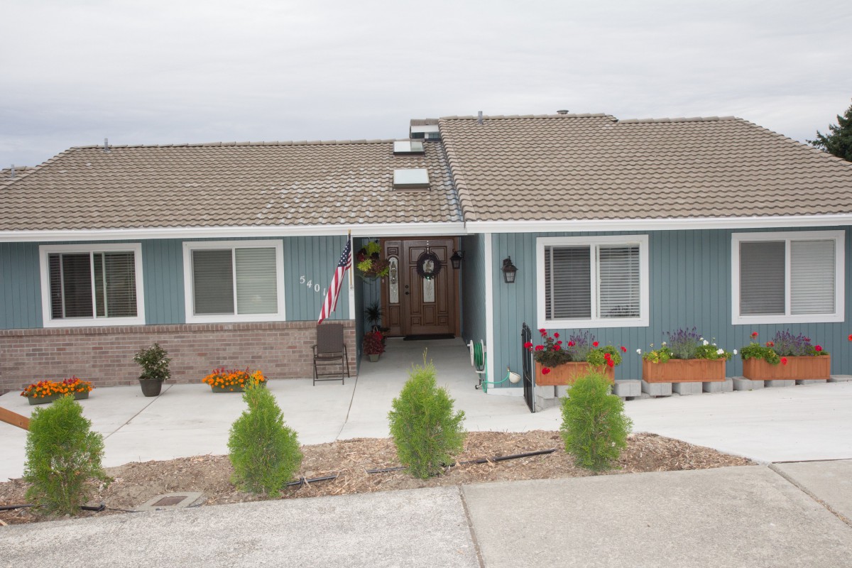 A bungalow-style house with a front yard and driveway, featuring an American flag and potted plants.