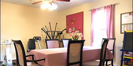 A dining room with a pink tablecloth, flowers, and exercise equipment in the corner.
