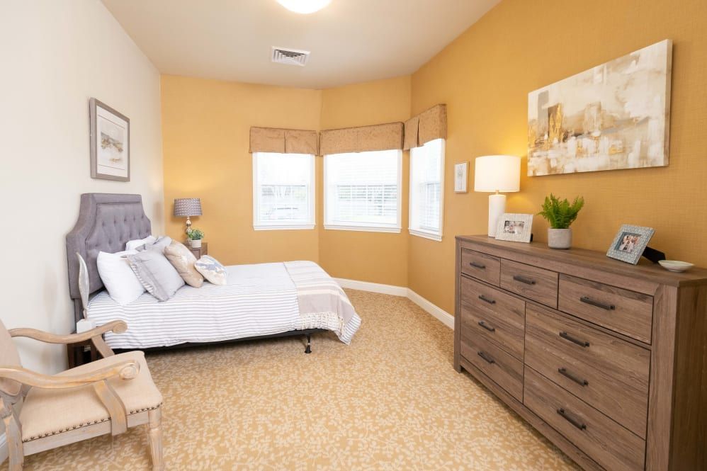 A cozy bedroom with warm yellow walls, featuring a comfortable bed and a wooden dresser.