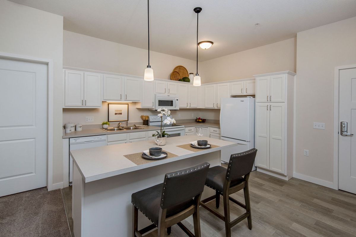 A modern kitchen with white cabinets, an island, and bar stools under pendant lighting.