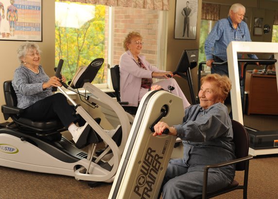 Elderly individuals exercising in a fitness facility using various machines.