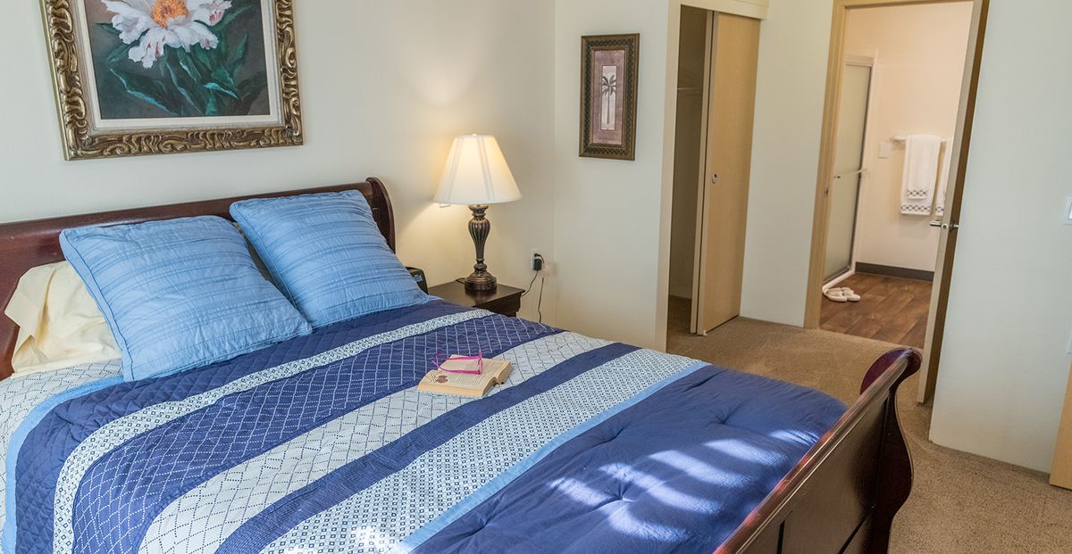 A cozy bedroom with a neatly made bed featuring blue bedding, a bedside lamp, and a book placed on the bed.