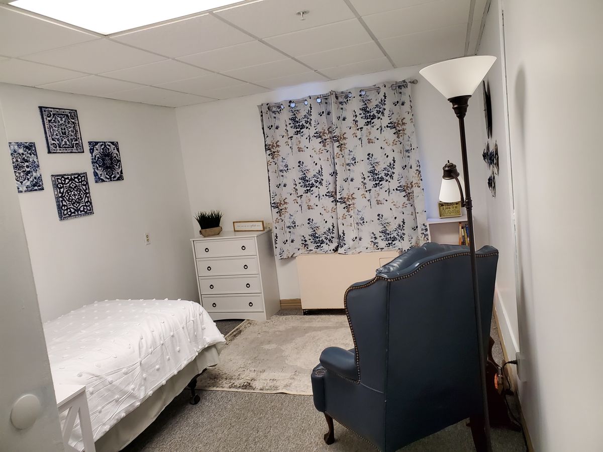 A cozy bedroom with a bed, chair, and dresser, decorated with floral curtains.