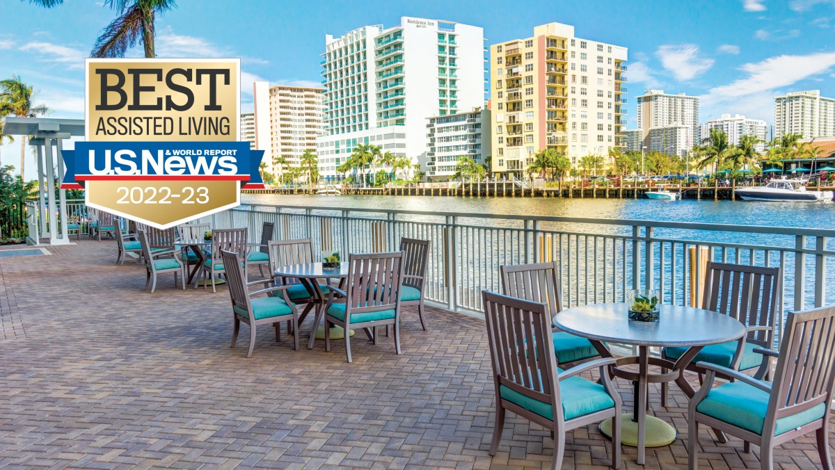A scenic outdoor dining area by the waterfront with high-rise buildings in the background.