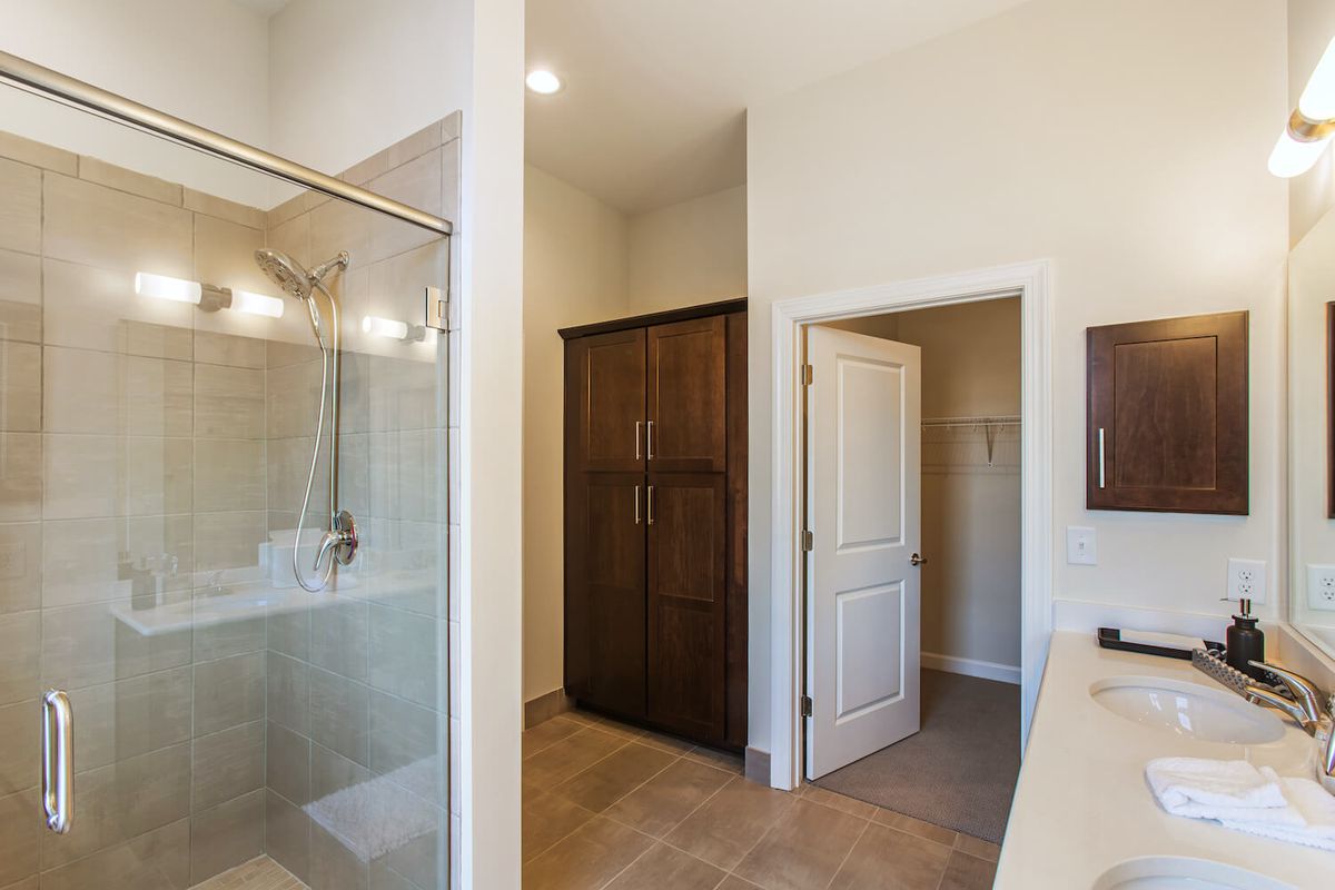 A modern bathroom featuring a glass shower enclosure, a large wooden cabinet, and tiled flooring.