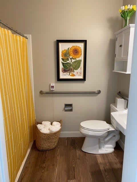 A cozy bathroom featuring a sunflower artwork and yellow shower curtain.