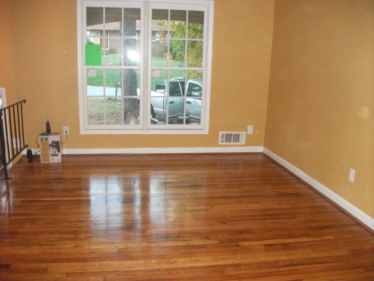 An empty room with a polished hardwood floor and a large window.