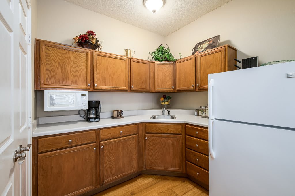 A cozy kitchen corner with wooden cabinets, a refrigerator, microwave, and coffee maker.