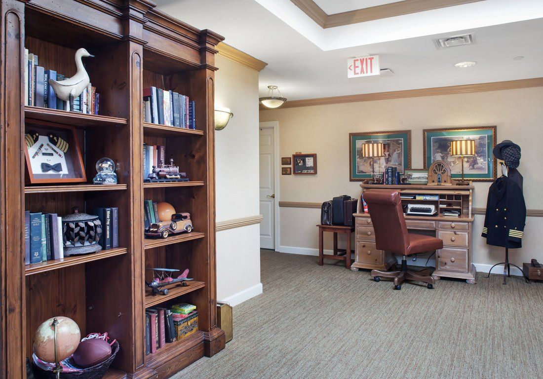 A cozy office space with a wooden bookshelf and desk, featuring decorative items and comfortable seating.