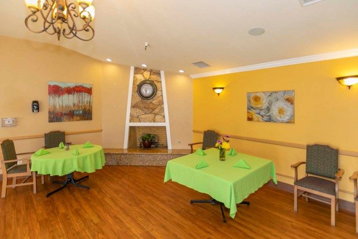 A cozy dining area with green tablecloths, a fireplace, and decorative art on yellow walls.