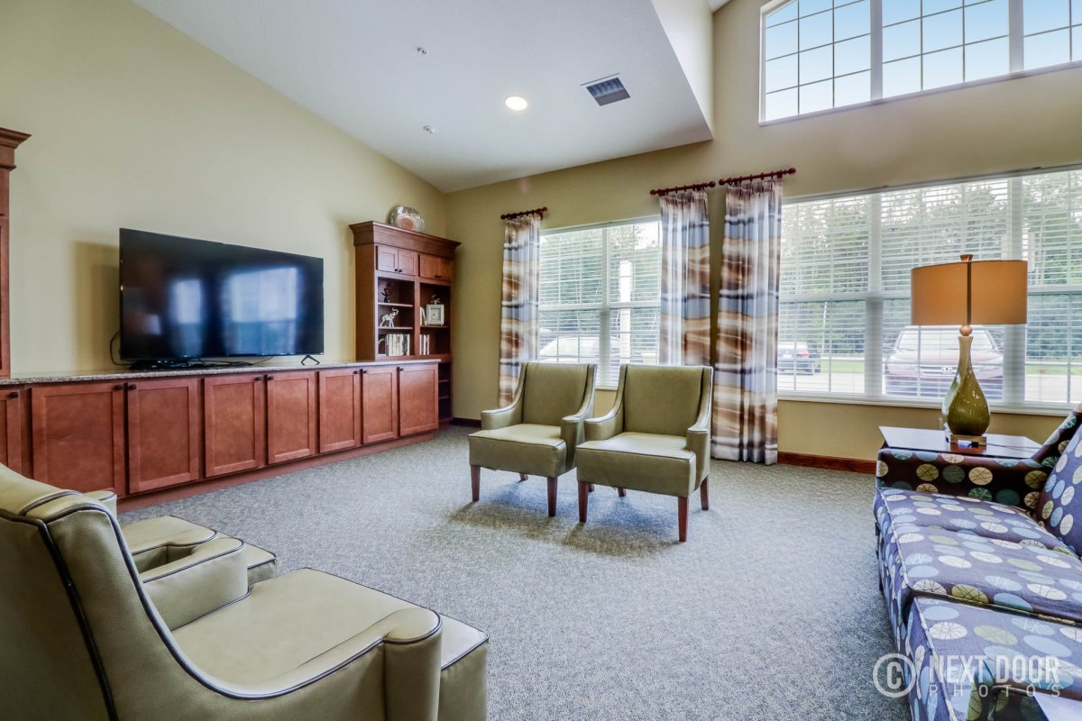 A spacious and cozy living room featuring a large TV, comfortable seating, and ample natural light from the large windows.