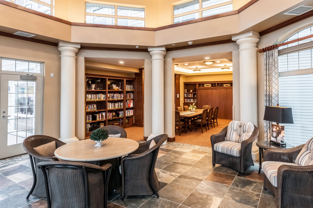 A cozy library with bookshelves, a reading area, and classic columns surrounding a round table.