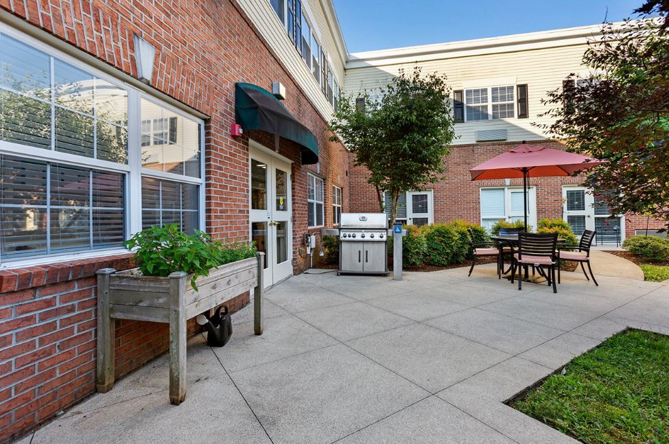 A cozy outdoor patio area with a grill and seating, adjacent to a brick building.