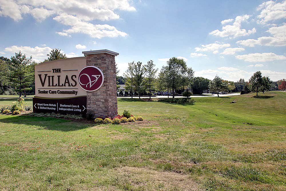 Entrance sign for The Villas at a residential complex surrounded by grass and trees under a blue sky.
