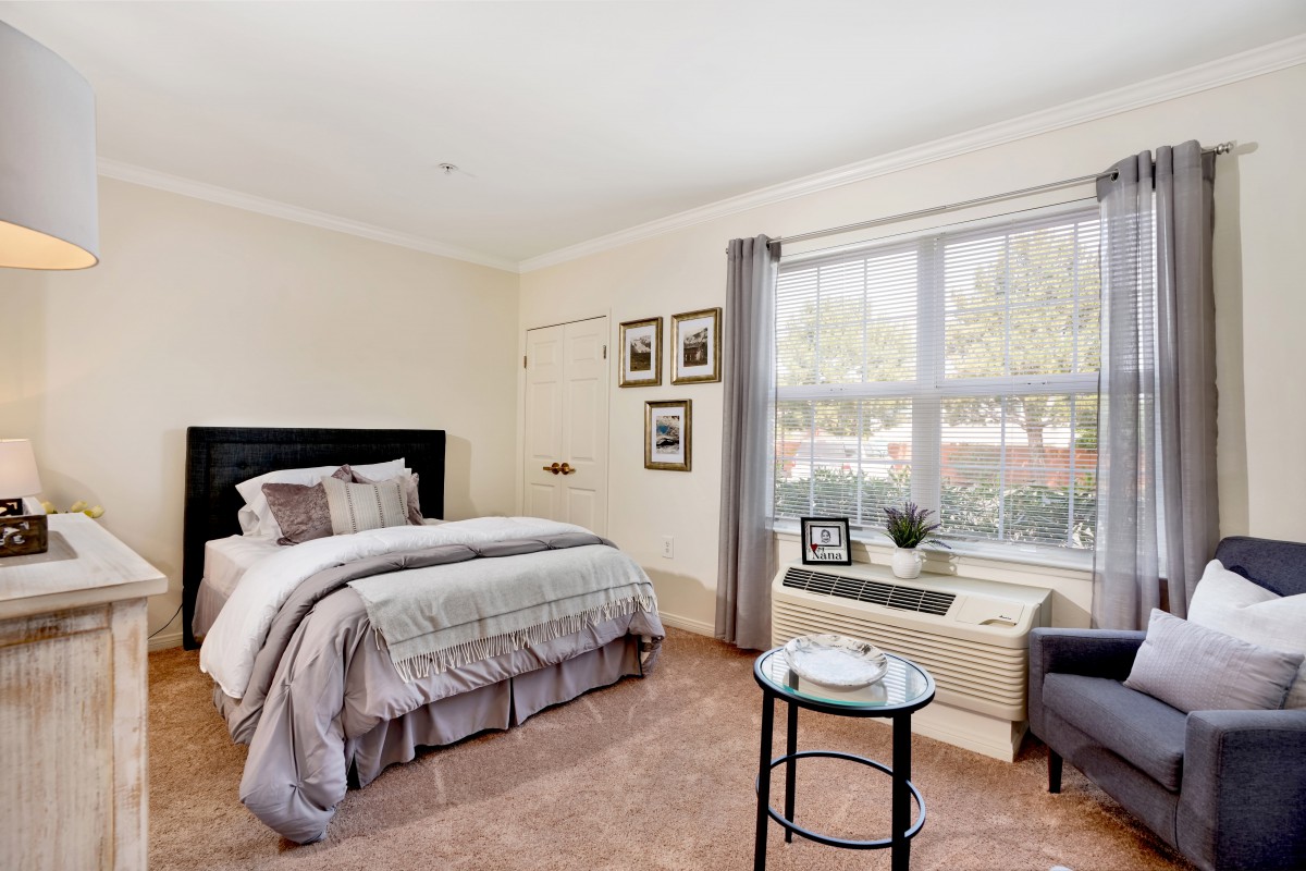 A cozy bedroom with a neatly made bed, large window, and simple decor.