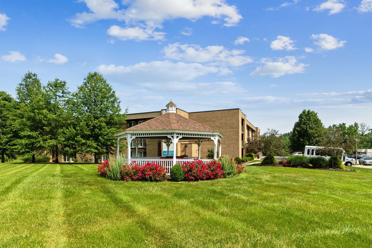 A well-maintained lawn with a gazebo and brick building under a partly cloudy sky.