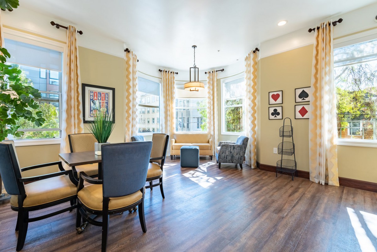 A well-lit living room with chairs around a table, large windows with curtains, and stylish decor.
