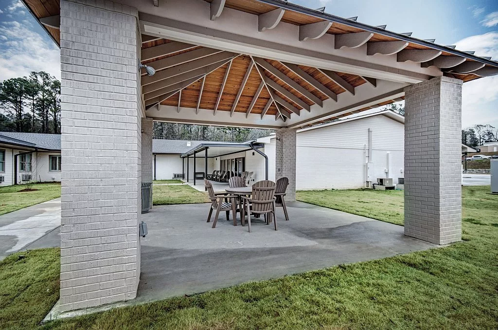 A covered outdoor patio featuring a dining set with a wooden ceiling and an open yard.