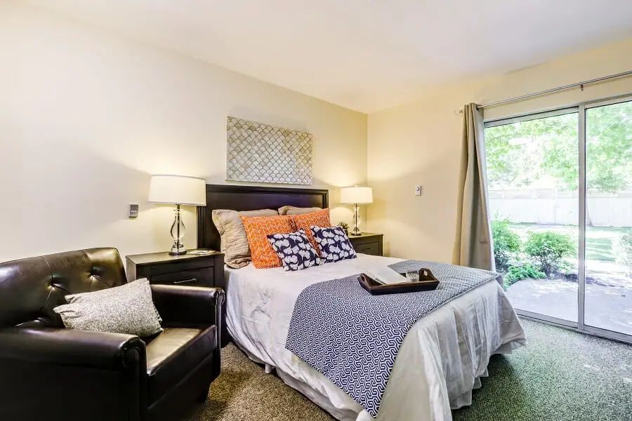 A modern bedroom with a comfortable bed and cozy armchair, featuring stylish decor and ample natural light.