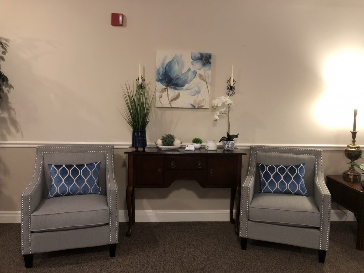 A cozy seating area with two gray chairs, accent cushions, and a decorative console table adorned with plants and artwork.