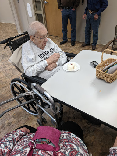 An elderly person enjoying dessert at a social gathering in a care facility.