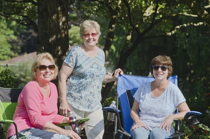 Three women enjoying a sunny day outdoors, sitting and smiling together.