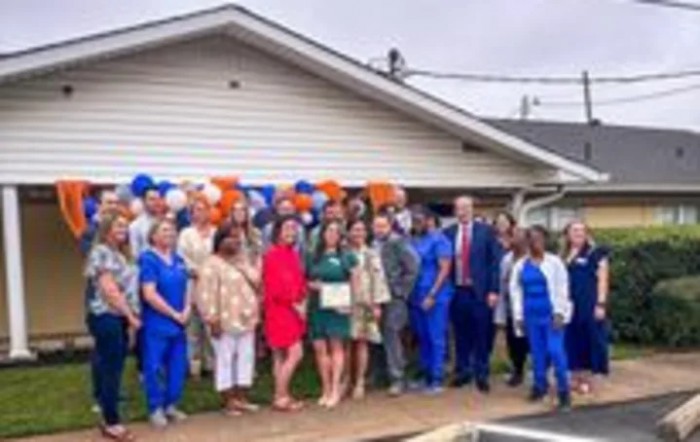 A group of people posing for a photo outside in front of a house with balloons in the background.