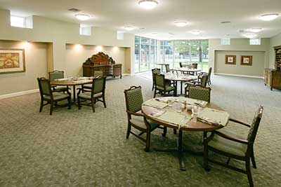 A spacious dining room with round tables and chairs, featuring a carpeted floor.