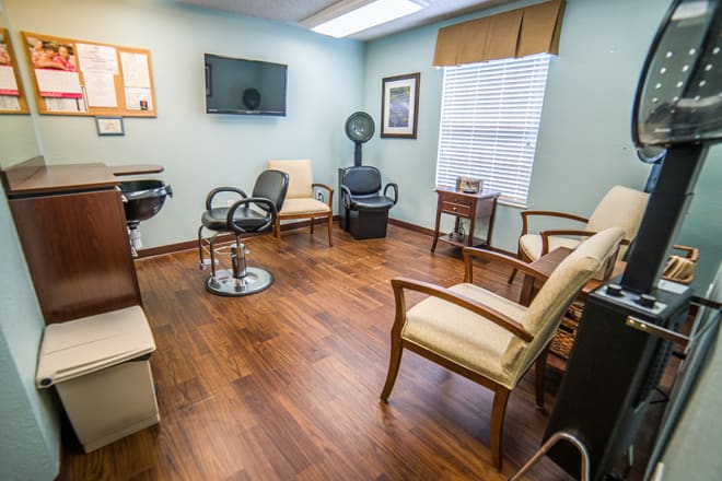 A cozy waiting room with wooden floors, featuring chairs and a TV.