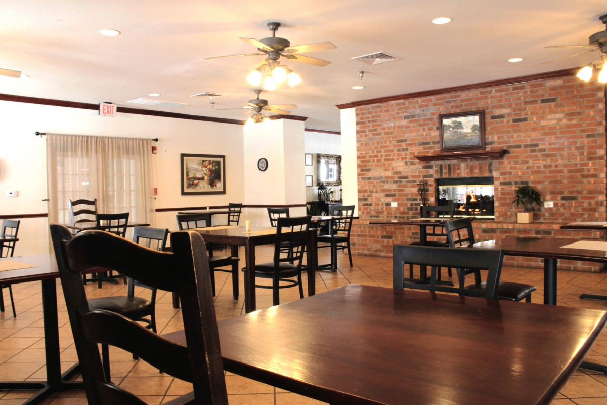 A cozy restaurant interior with wooden tables and chairs, brick wall, and ceiling fans.