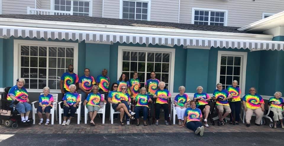 A group of people wearing colorful tie-dye shirts gather for a casual outdoor photo.