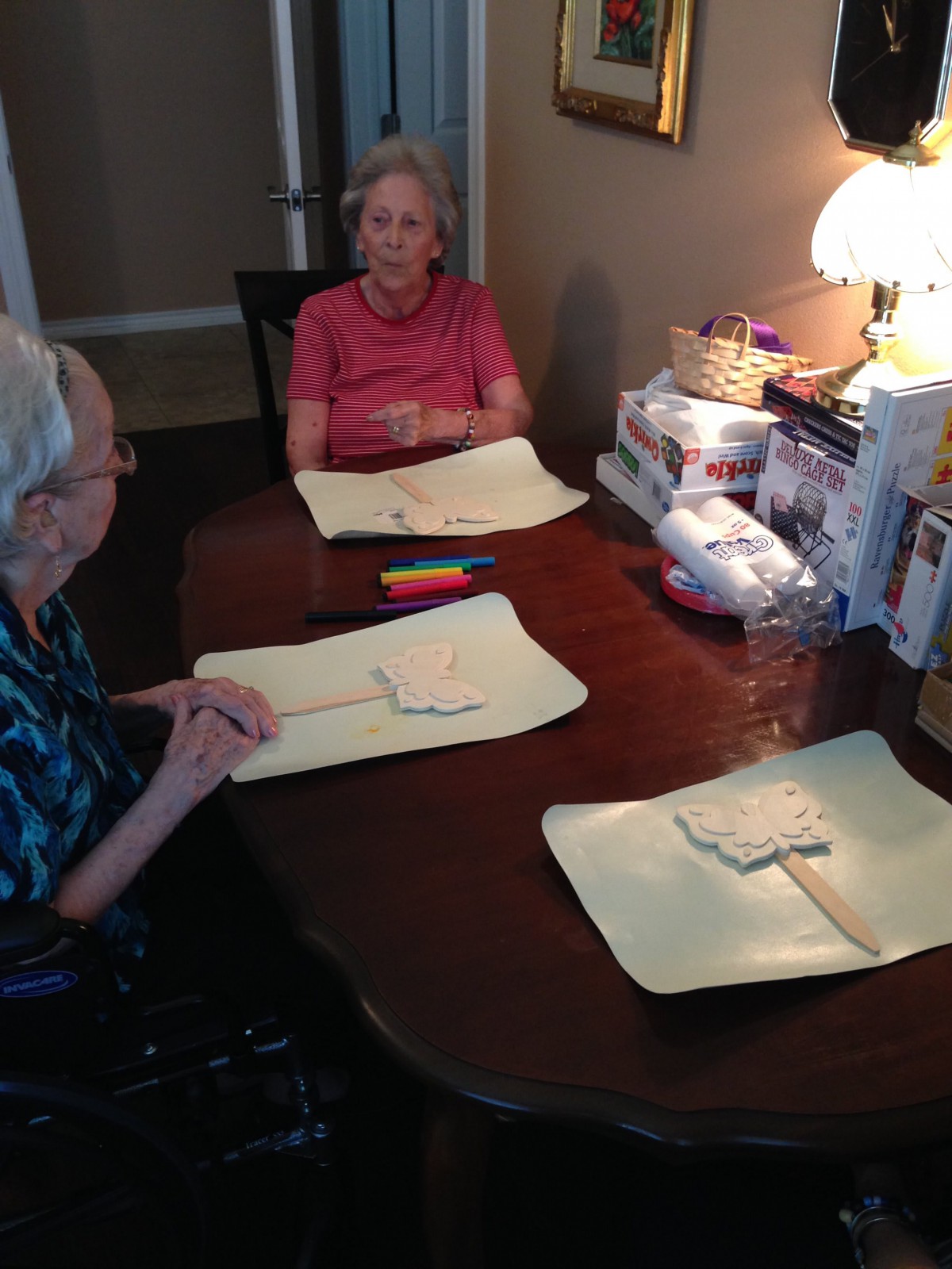 Two senior women sitting at a table with crafts, engaged in conversation.