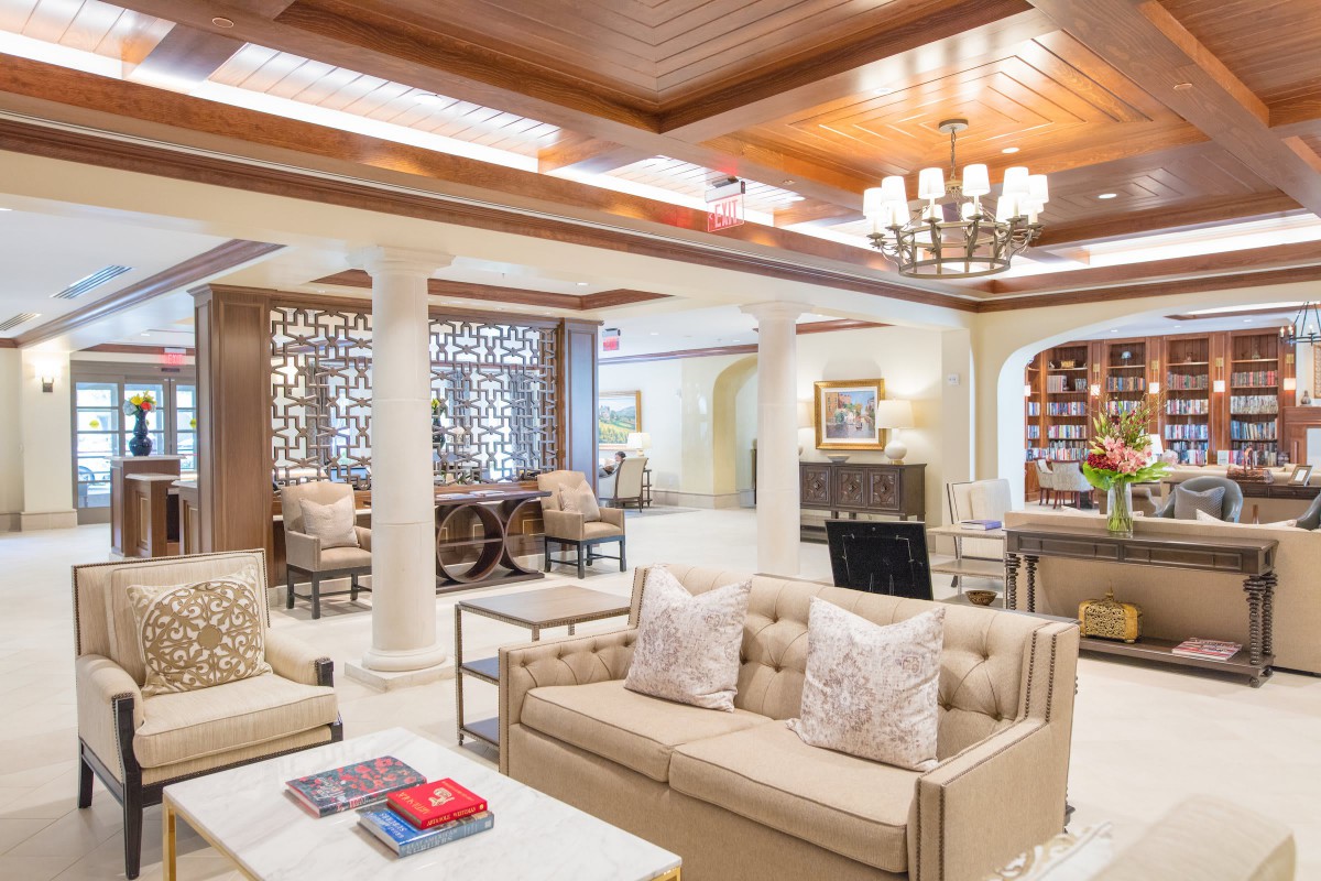 A luxurious and elegantly designed living room with plush sofas, a chandelier, decorative columns, and a bookshelf.