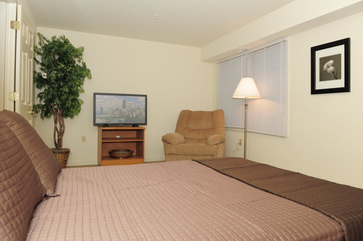 A cozy bedroom with a bed, chair, TV, and lamp.