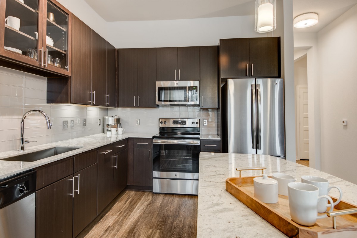 A modern kitchen featuring stainless steel appliances and dark wood cabinetry, complemented by a sleek countertop and stylish lighting.