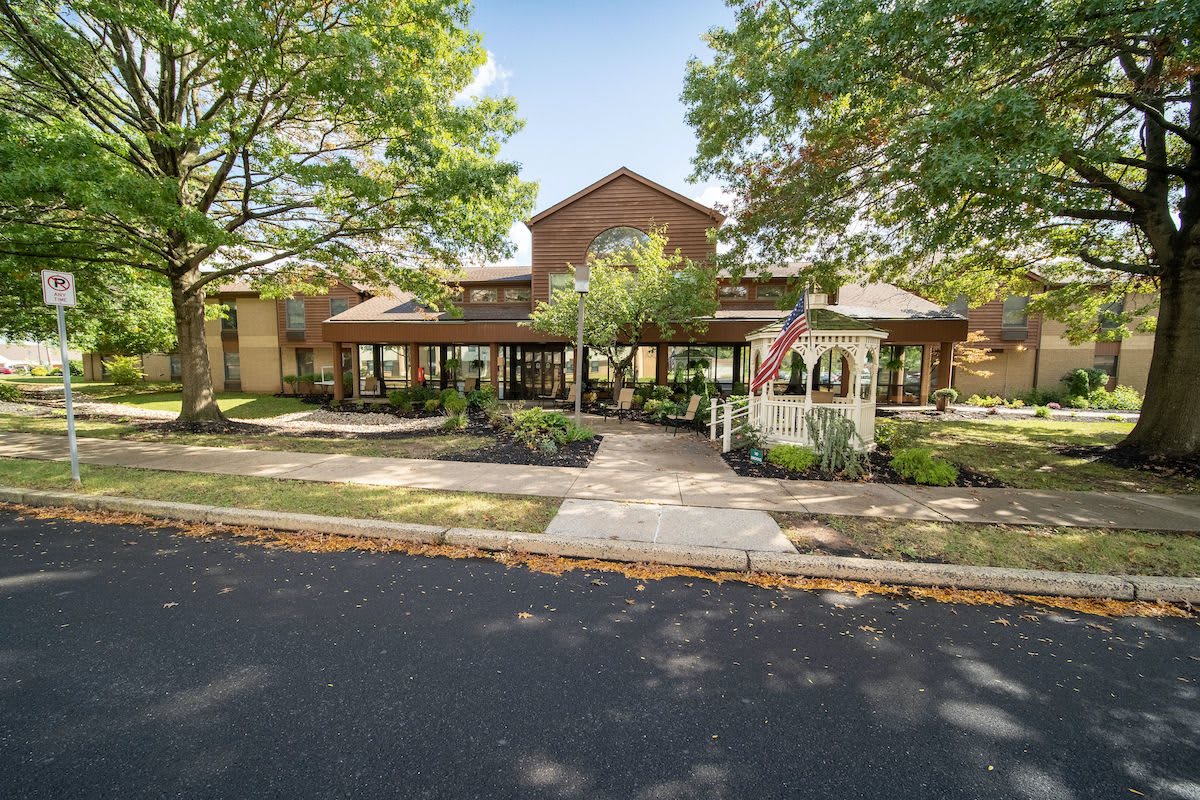 A front view of a building with a well-maintained garden and pathway, surrounded by trees during the daytime.