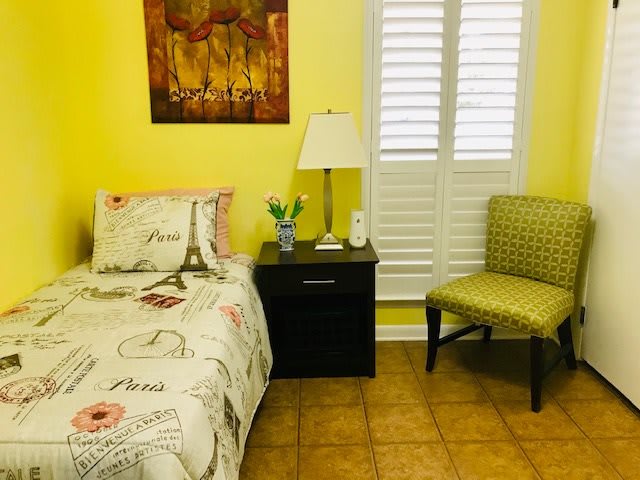 Cozy bedroom with yellow walls and a single bed, featuring a nightstand and decorative elements.