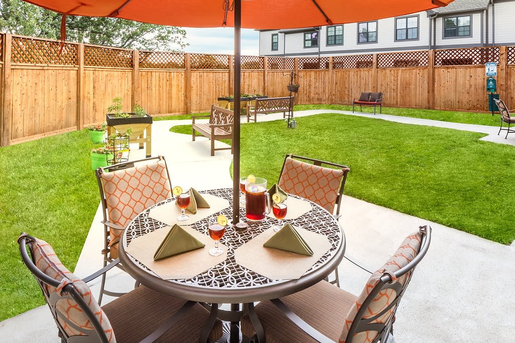A cozy outdoor dining area with a table and chairs under an umbrella, set in a well-maintained backyard.
