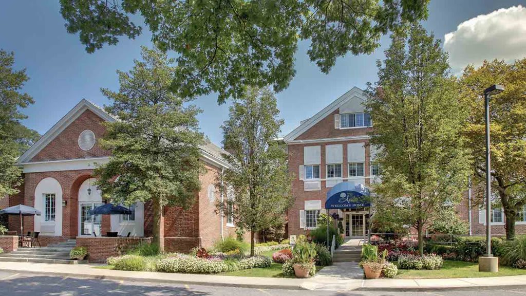 A well-maintained building surrounded by lush trees and landscaping under a clear summer sky.