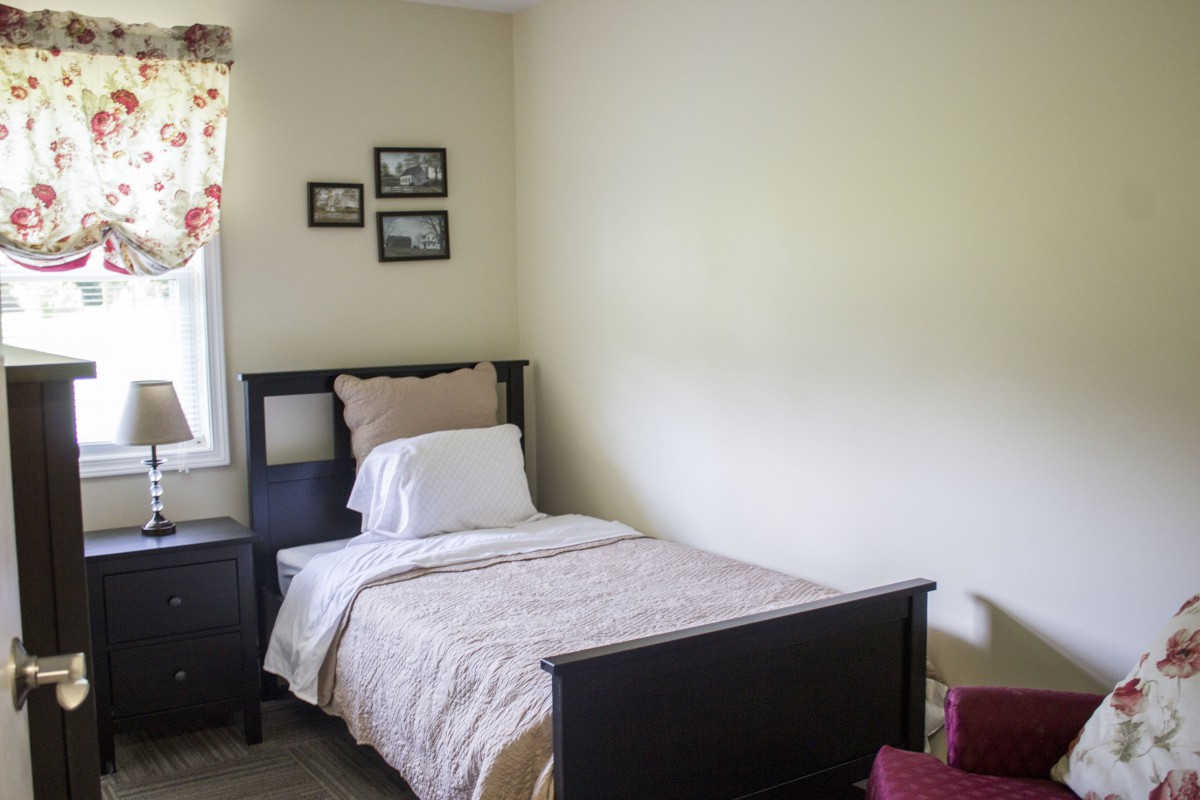 A cozy and simple bedroom with a single bed, nightstand, and pictures hanging on the wall.