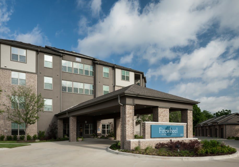 A modern hotel building with a covered entrance and a cloudy sky background.