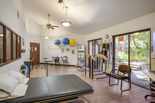 A well-equipped therapy room featuring exercise balls, various chairs, and rehabilitation tools.