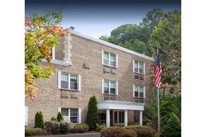 A brick building with multiple windows, surrounded by trees and an American flag in front.
