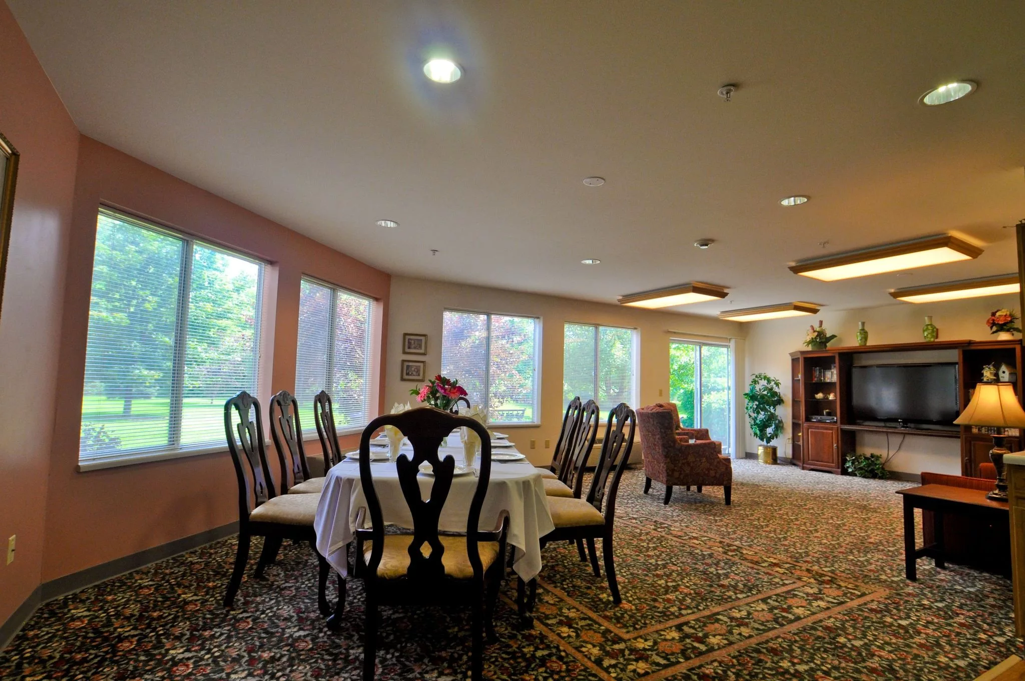 A spacious dining room with a large table surrounded by chairs, featuring large windows and elegant decor.