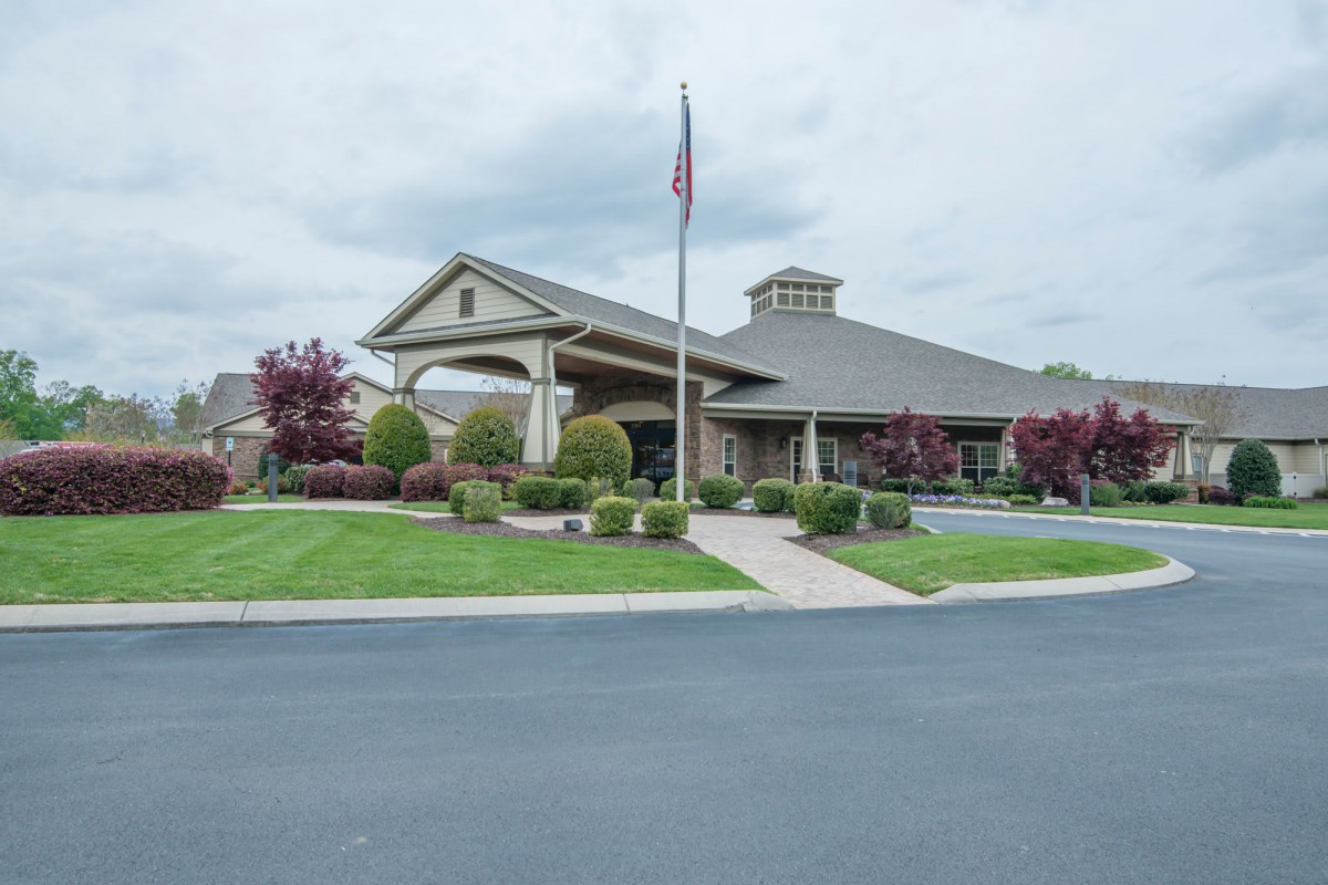 A well-maintained building with a landscaped front, featuring a flagpole and a parking area under a cloudy sky.