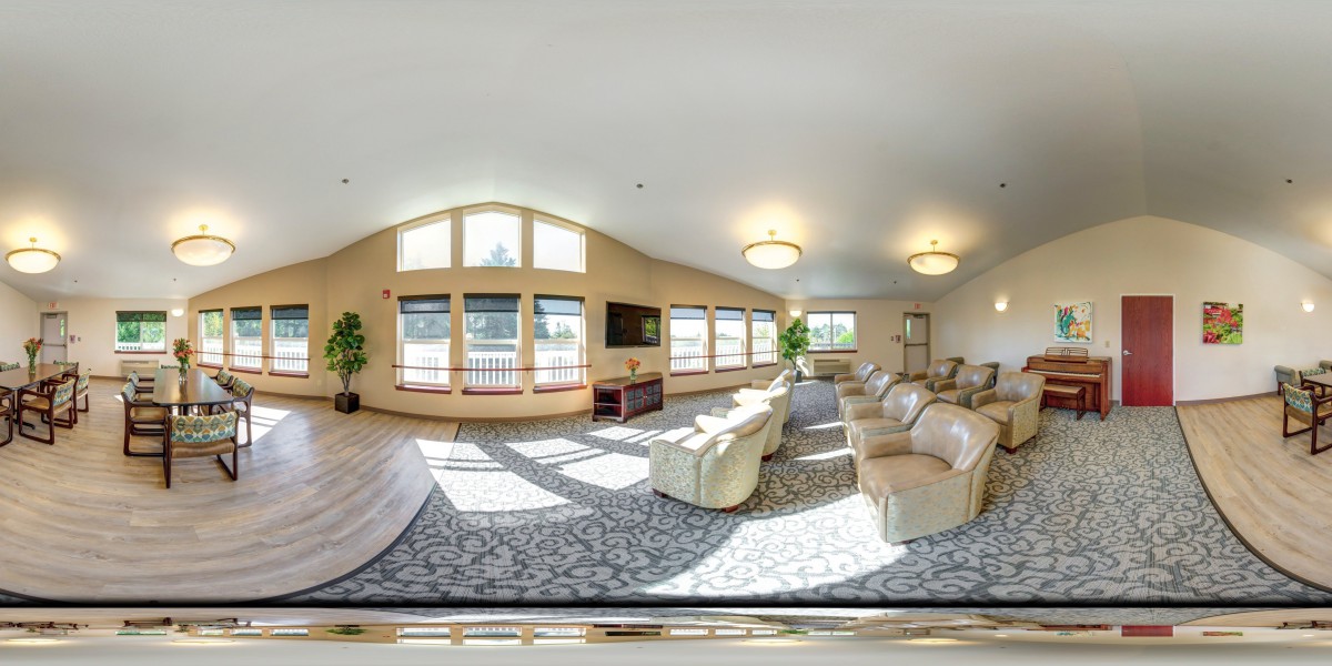 A spacious living room with ample seating, large windows, and a TV, lit by ceiling lights.