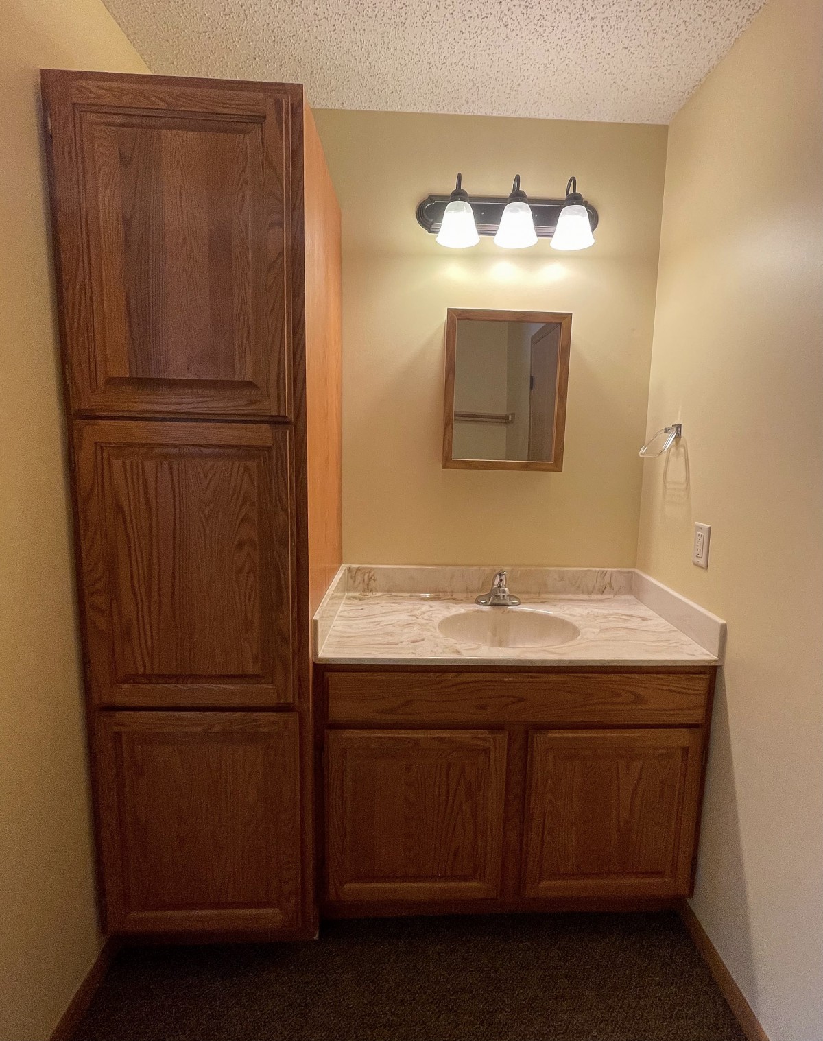 A bathroom vanity with wooden cabinets, a mirror, and overhead lighting.